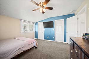 Carpeted bedroom featuring a textured ceiling, ceiling fan, and vaulted ceiling