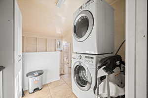 Laundry room featuring light tile patterned flooring, stacked washer and dryer, and wooden walls