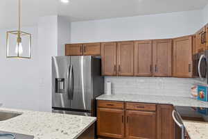 Kitchen featuring hanging light fixtures, light stone countertops, backsplash, and appliances with stainless steel finishes