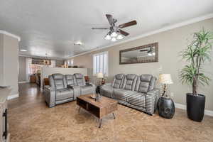 Living room with ceiling fan with notable chandelier, a healthy amount of sunlight, ornamental molding, and a textured ceiling