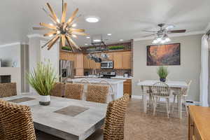 Tiled dining space featuring ceiling fan with notable chandelier and crown molding