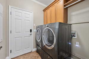 Clothes washing area featuring washer and clothes dryer, cabinets, ornamental molding, and light tile patterned floors