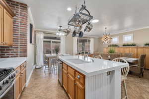 Kitchen featuring ornamental molding, stainless steel appliances, a kitchen island with sink, sink, and pendant lighting