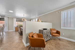 Living area with ceiling fan with notable chandelier, light tile patterned flooring, ornamental molding, and a textured ceiling