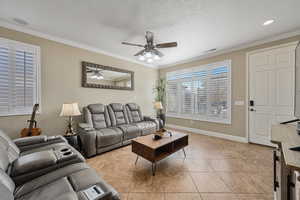 Tiled living room featuring a textured ceiling, ceiling fan, and ornamental molding