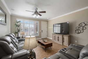 Living room featuring a textured ceiling, ceiling fan, light tile patterned floors, and crown molding