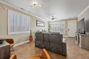 Living room with light tile patterned floors, a textured ceiling, ceiling fan, and crown molding