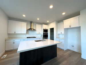 Kitchen featuring a kitchen island with sink, white cabinets, sink, wall chimney exhaust hood, and appliances with stainless steel finishes