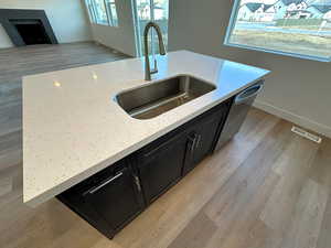 Kitchen featuring light stone counters, sink, stainless steel dishwasher, and light hardwood / wood-style flooring