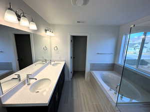 Bathroom featuring a textured ceiling, vanity, and tiled bath