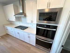 Kitchen featuring white cabinets, built in microwave, wall chimney exhaust hood, and gas stovetop