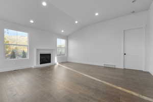 Unfurnished living room featuring wood-type flooring, vaulted ceiling, and a healthy amount of sunlight