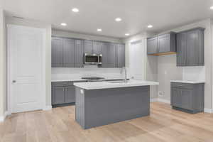 Kitchen featuring sink, gray cabinets, light hardwood / wood-style flooring, and an island with sink