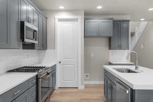 Kitchen with decorative backsplash, appliances with stainless steel finishes, gray cabinetry, and sink