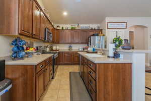 Kitchen with sink, a kitchen bar, a center island with sink, light tile patterned floors, and appliances with stainless steel finishes