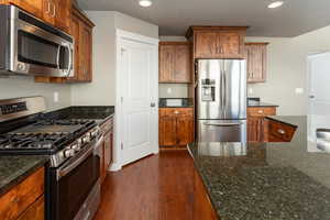 Kitchen featuring dark hardwood / wood-style floors, dark stone countertops, and appliances with stainless steel finishes