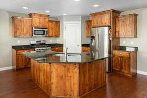 Kitchen featuring a kitchen island with sink, dark wood-type flooring, sink, dark stone countertops, and appliances with stainless steel finishes