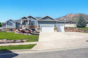 Craftsman-style home featuring a garage, board and batten siding, stone siding, a front yard, and driveway