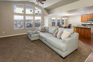 Living room featuring vaulted ceiling, sink, dark wood-type flooring, and ceiling fan with notable chandelier