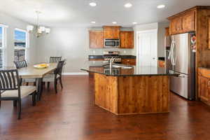 Kitchen with appliances with stainless steel finishes, a kitchen island with sink, sink, decorative light fixtures, and a notable chandelier