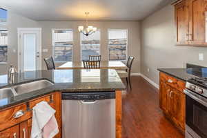 Kitchen featuring hanging light fixtures, stainless steel appliances, dark hardwood / wood-style flooring, dark stone counters, and a chandelier