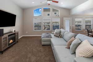 Living room with a wealth of natural light, dark carpet, ceiling fan, and lofted ceiling