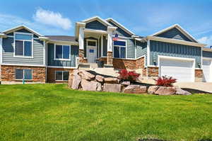 View of front of house featuring stone siding, board and batten siding, a front lawn, and concrete driveway