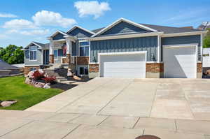 View of front facade with board and batten siding, stone siding, an attached garage, driveway, and a porch