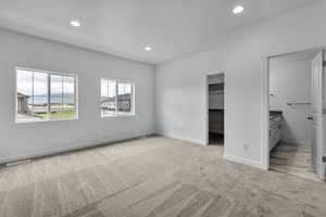 Unfurnished bedroom with ensuite bathroom, a walk in closet, light carpet, and a closet