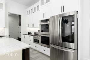 Kitchen featuring decorative backsplash, dark stone countertops, white cabinetry, and appliances with stainless steel finishes