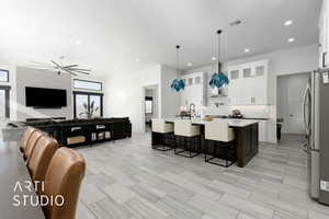 Kitchen with white cabinetry, stainless steel fridge, decorative light fixtures, a breakfast bar, and a center island with sink