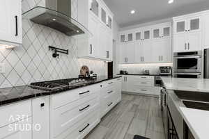 Kitchen featuring white cabinetry, wall chimney exhaust hood, dark stone counters, and appliances with stainless steel finishes