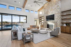 Living room featuring a stone fireplace, a towering ceiling, beamed ceiling, and light hardwood / wood-style floors