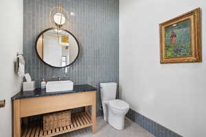 Bathroom featuring tile patterned flooring, vanity, tile walls, and toilet