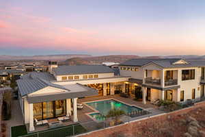 Back house at dusk with a mountain view, a patio, a fenced in pool, and a balcony