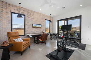 Workout area featuring ceiling fan, a healthy amount of sunlight, and brick wall