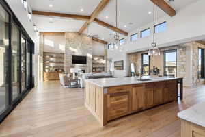 Kitchen with ceiling fan with notable chandelier, sink, a large island with sink, decorative light fixtures, and high vaulted ceiling