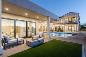 Back house at dusk featuring a patio, a balcony, and an outdoor fire pit