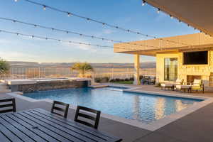 View of pool with an outdoor hot tub, pool water feature, an outdoor living space with a fireplace, a patio area, and a mountain view