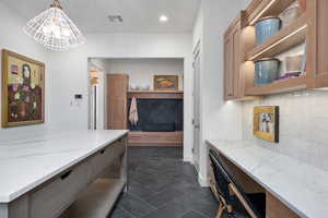 Kitchen featuring tasteful backsplash, light stone countertops, pendant lighting, and an inviting chandelier