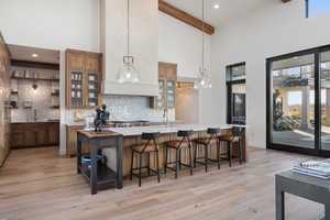 Kitchen with light hardwood / wood-style flooring, beamed ceiling, a towering ceiling, decorative light fixtures, and decorative backsplash