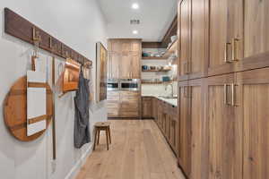 Bar with light wood-type flooring, stainless steel oven, backsplash, and sink