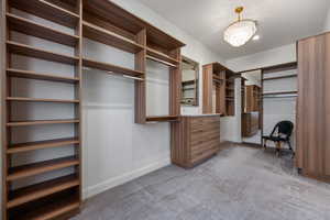 Spacious closet featuring dark colored carpet and a notable chandelier