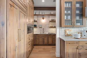 Kitchen featuring backsplash, sink, stainless steel oven, and light hardwood / wood-style floors