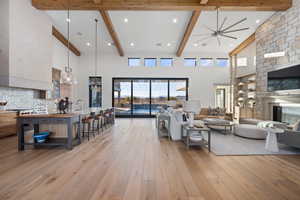 Living room featuring beam ceiling, a large fireplace, light hardwood / wood-style flooring, a towering ceiling, and ceiling fan with notable chandelier