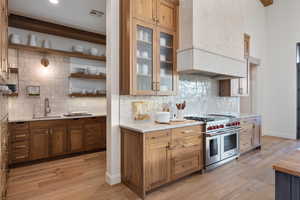 Kitchen featuring custom exhaust hood, double oven range, light wood-type flooring, and sink