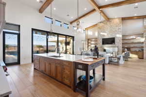 Kitchen featuring ceiling fan, sink, high vaulted ceiling, beamed ceiling, and a stone fireplace