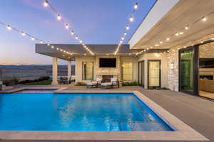 Pool at dusk featuring an outdoor stone fireplace and a patio area