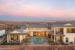 Back house at dusk with a mountain view, a patio, a fenced in pool, and a balcony