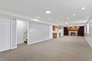 Unfurnished living room with carpet flooring, built in shelves, and a stone fireplace